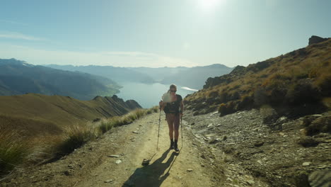 mujer activa en forma caminando por un sendero empinado de montaña hacia el pico del istmo, sol brillante