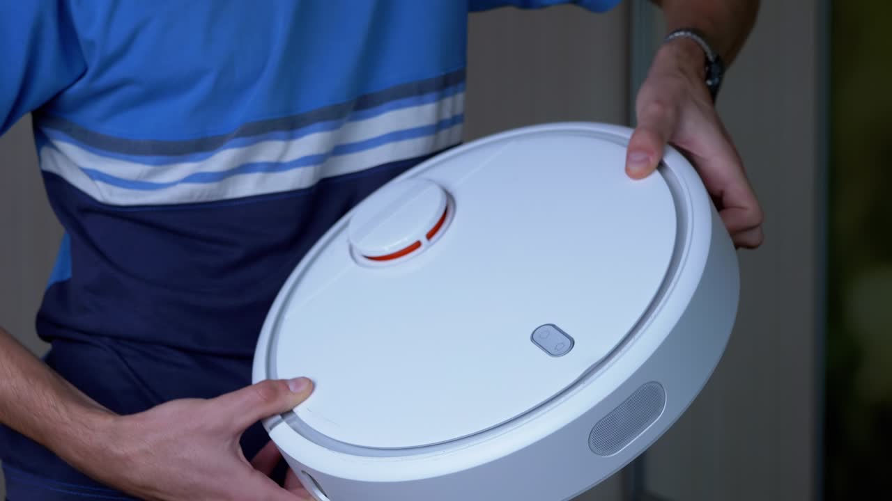 hombre sostiene en las manos un robot aspirador automático recién comprado. 4k. de cerca