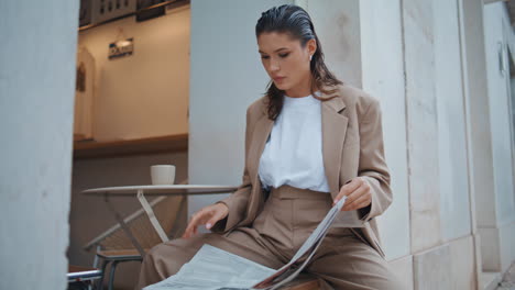 woman turning pages newspaper in cozy outdoors restaurant close up. elegant lady