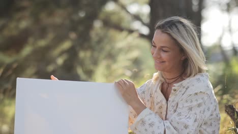 a woman fully engaged in the beautiful process of creating art outdoors on a blank canvas a joyful woman thoughtfully and carefully prepares a blank canvas in the beautiful nature for her artistic expression
