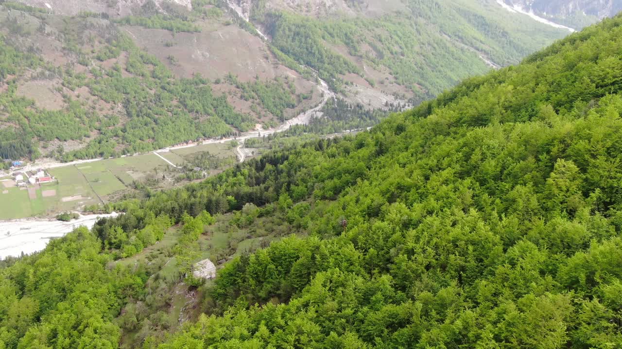 vista de avión no tripulado en albania volando en los alpes mostrando bosque verde en un valle rodeado de montañas con picos nevados en valbon?