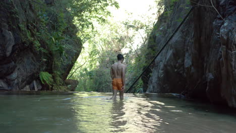 Hombre-Caminando-En-Aguas-Profundas-Hasta-La-Cintura-En-Una-Cascada-Aislada-En-La-Jungla,-Antena