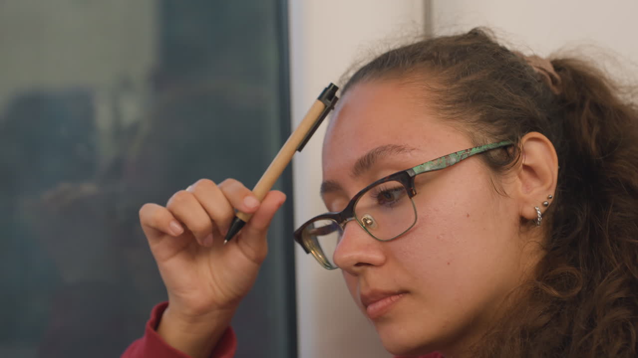 Aspirante romanziere contempla la trama accanto al finestrino del treno, con la penna appoggiata alla fronte, gli occhiali che riflettono la luce del crepuscolo, sguardo pensieroso verso lo skyline, una tranquilla pausa creativa, brainstorming interiore.
