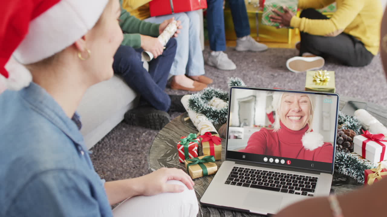 산타 모자를 가진 다양한 친구들이 행복한 백인 여성과 노트북 비디오 통화를 하고 있습니다.