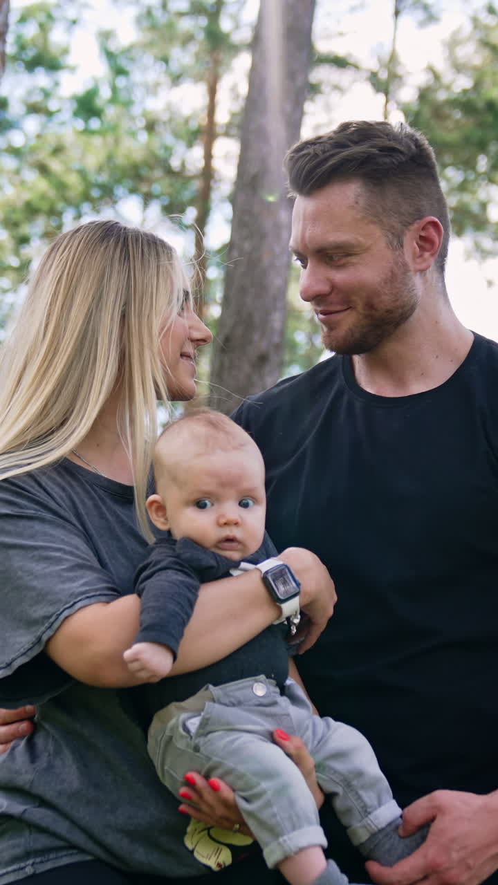 Beautiful Caucasian couple with their child stand together. Happy parents spend good time all together in the forest. Low angle view. Vertical video