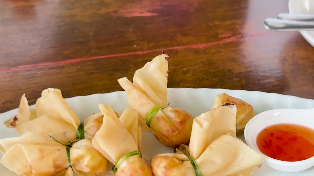Un piatto bianco di wonton fritti croccanti con salsa da intingere su legno