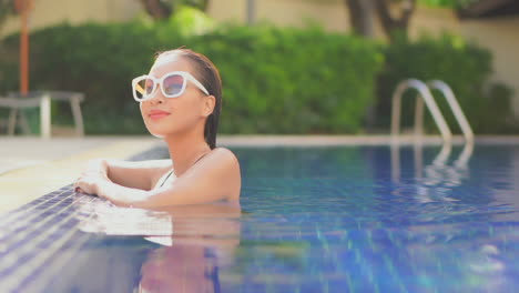 beautiful young asian woman with big sunglasses relaxing in pool