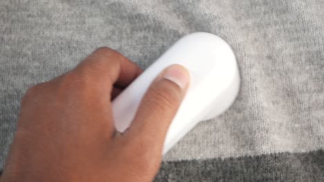 person using a handheld lint remover on a gray sweater