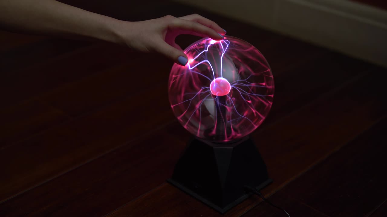 una mano femenina toca una bola de plasma dando pequeños relámpagos. experimentos con electricidad en la oscuridad.