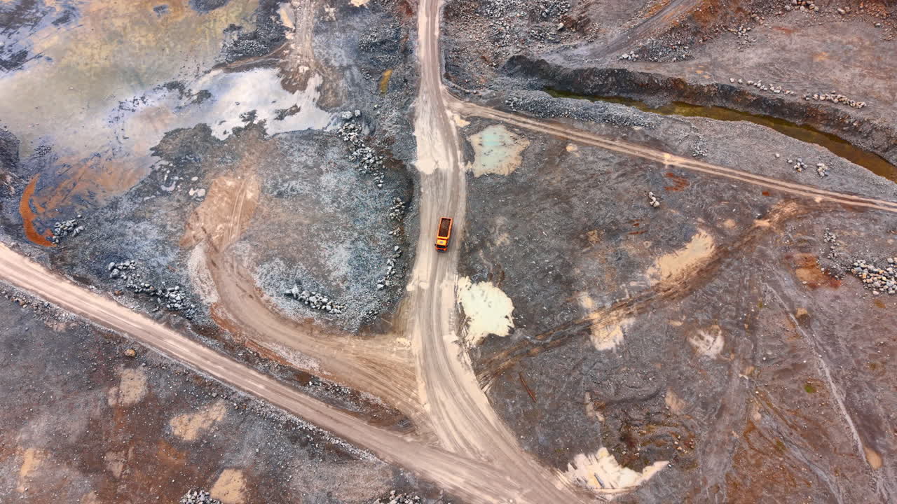 Truck drives on dirt road at mining site. A truck moves along a dirt road in a mining area with rocky ground and water pools nearby during the day