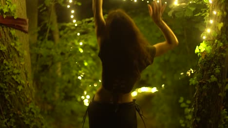 adorable young woman dancing on a forest nature surrounded by string lights at summer evening