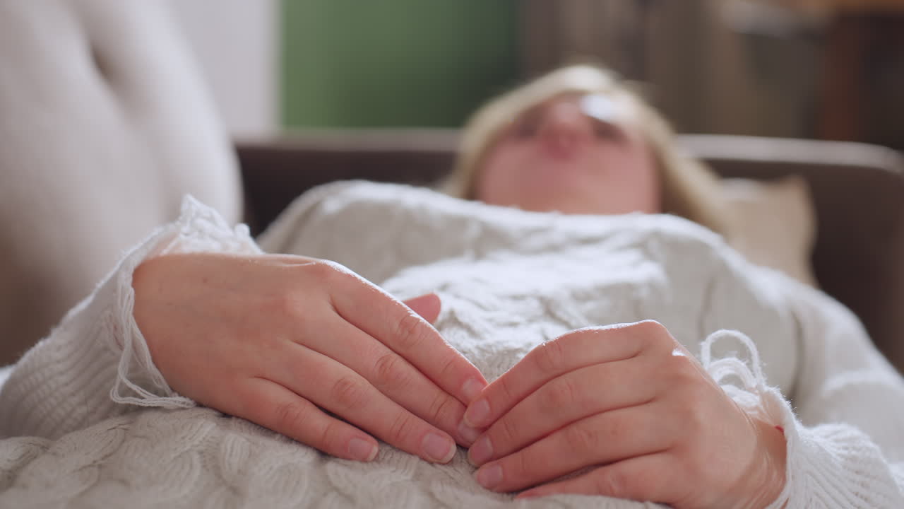 Vulnerable visitor lying on comfortable sofa touching her fingertips she breathes in and out in slow rhythm over soft knit blanket under gentle natural light during therapy session