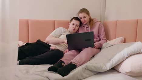 pareja relajándose en la cama, viendo la computadora portátil