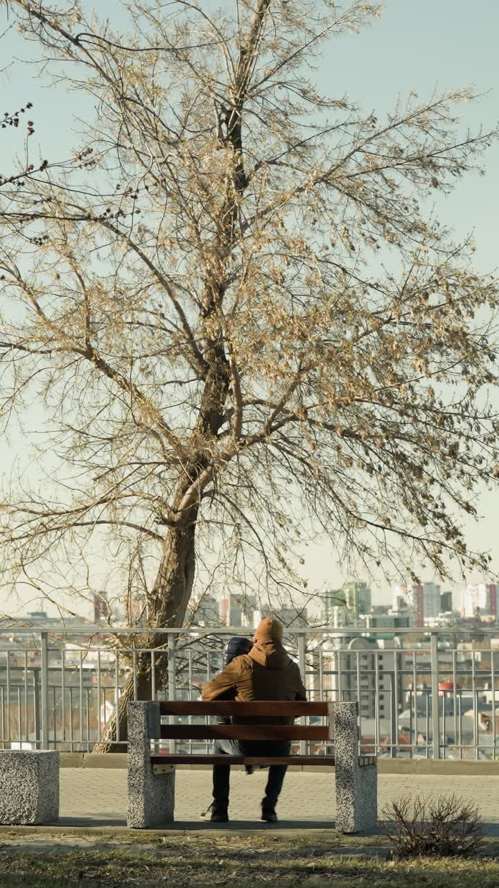 아들을 다리 위에 고 있는 아버지와 함께 공원 벤치에 앉아 도시 풍경을 바라보는 아버지가 벤치 위의 자세를 조정하면서