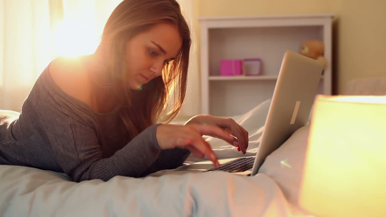 Pretty happy brunette lying on bed typing on laptop