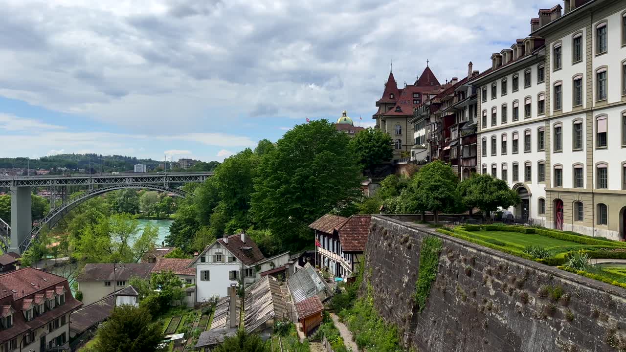 Aerial panning shot of ancient houses with river view and famous bridge of Bern in background. Historic buildings in city capital of Switzerland. Sunny day with clouds in summer. Panorama wide shot.