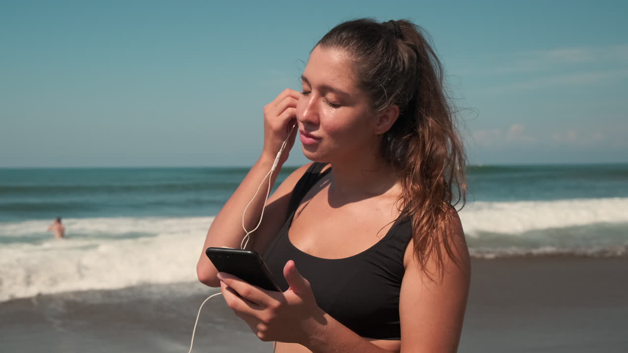 Woman Applying Sunscreen on the Beach, Listening to Music