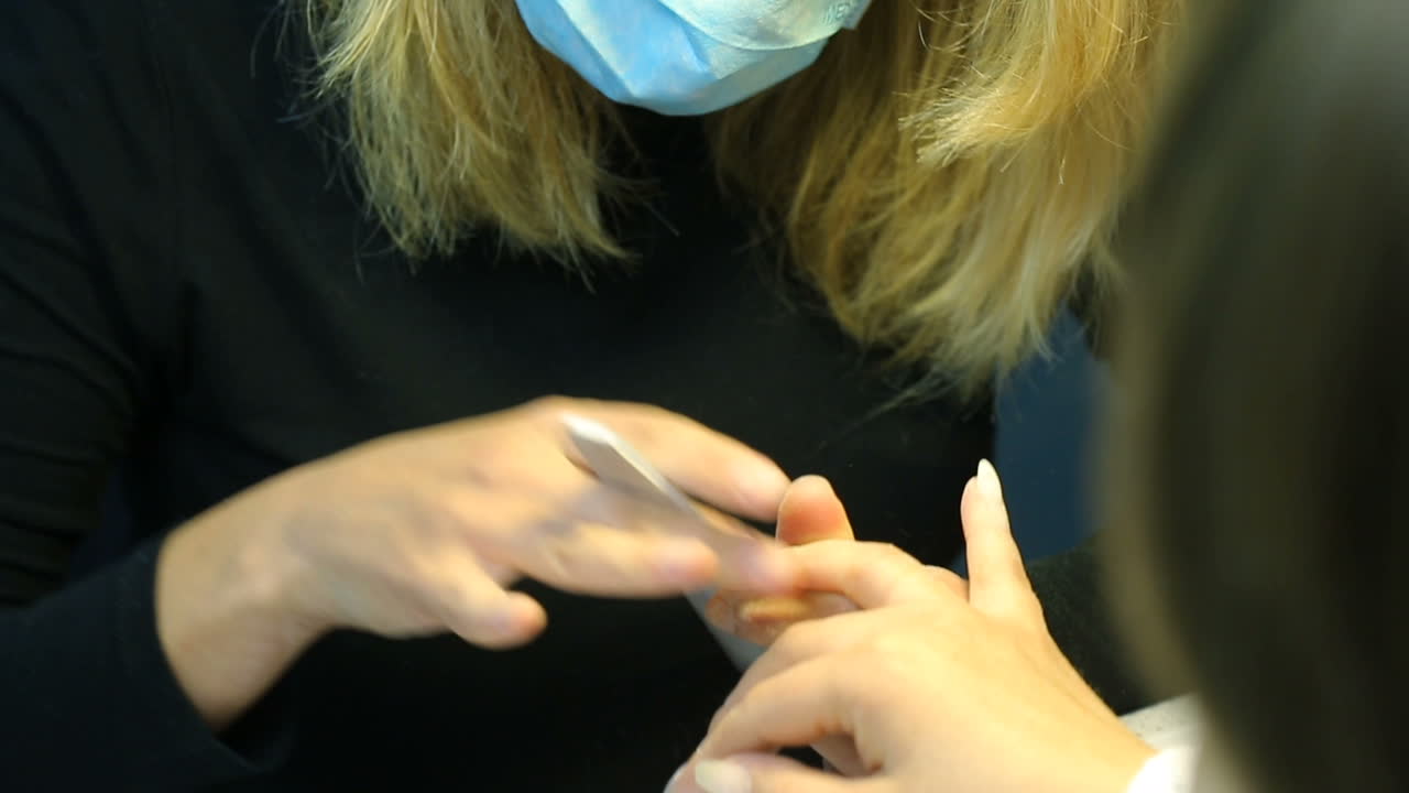 Woman in salon receiving manicure by nail beautician