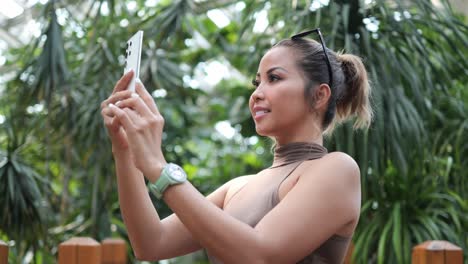 mujer sosteniendo un teléfono inteligente y tomando una foto de vegetación en un jardín botánico