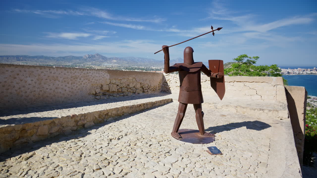 Steel sculpture of a medieval crossbowman on the Santa Barbara Castle parapet, city and mountains on the background