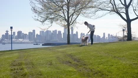 young woman plays with dog in front of vancouver skyline