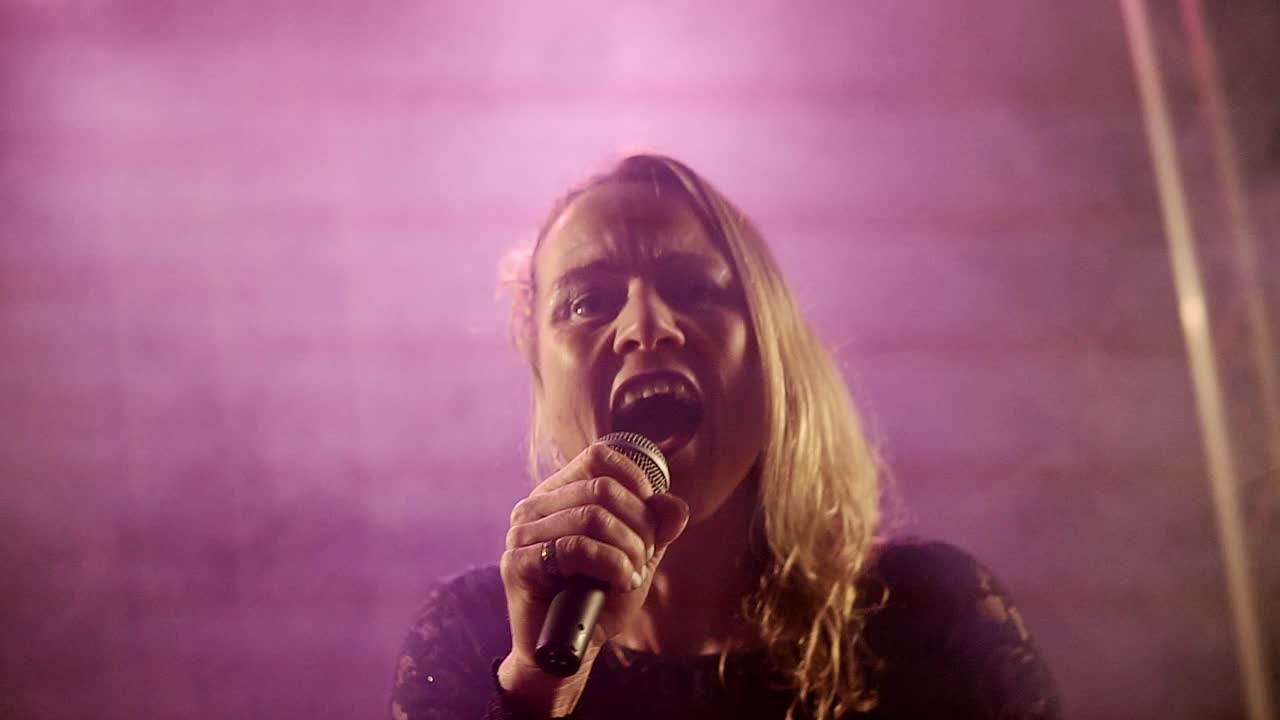 Backlit silhouette of singer vocalist girl with short hair standing in nightclub disco studio and start singing performance with mic in hand