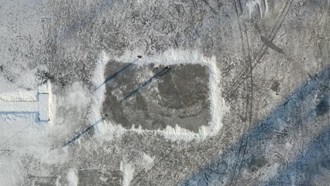 An-aerial-drone-shot-looking-straight-down-on-a-makeshift-ice-rink-on-a-large-frozen-lake-with-3-people-playing-with-a-ball---Daytime