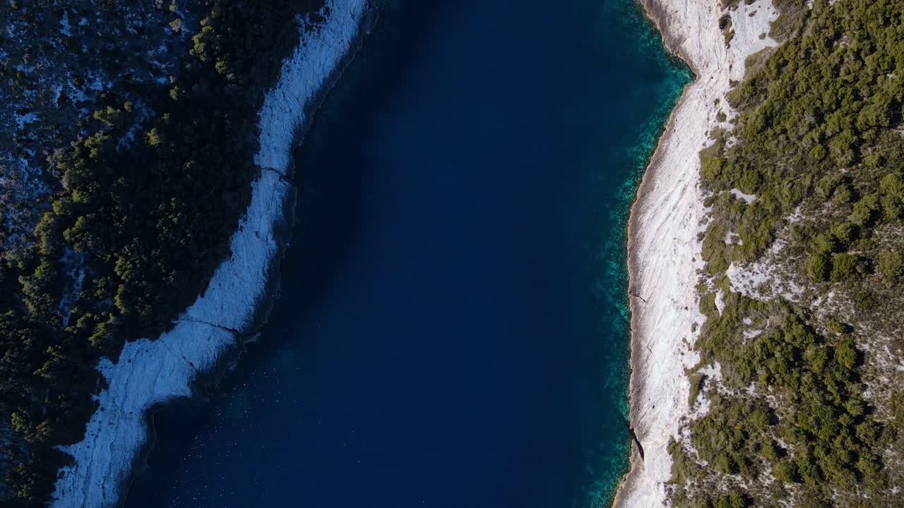 Ripresa aerea con drone delle acque blu scintillanti e della rigogliosa vegetazione verde, circondate su entrambi i lati da alte e ripide scogliere.