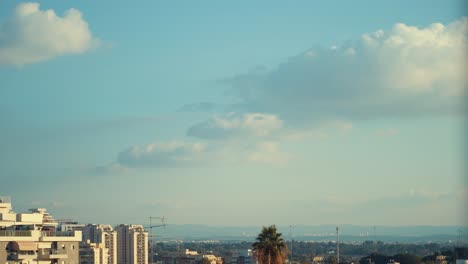 time lapse shot of a surfing clouds in the blue skies, green tree, cityscape and a palm tree in the background, 4k video