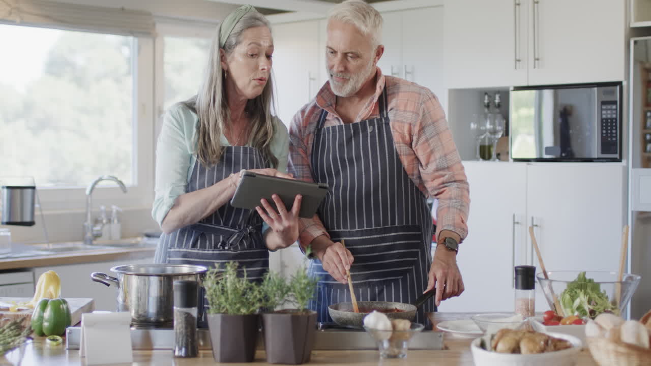 pareja caucásica de mediana edad con tableta, preparando comida, cocinando en la cocina en casa, cámara lenta