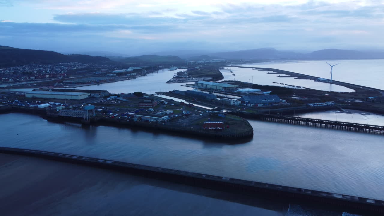 Veduta aerea in allontanamento del vasto porto di Swansea all'alba. Paesaggio industriale marittimo per l'attracco di carichi trasportati e la riparazione e manutenzione di imbarcazioni