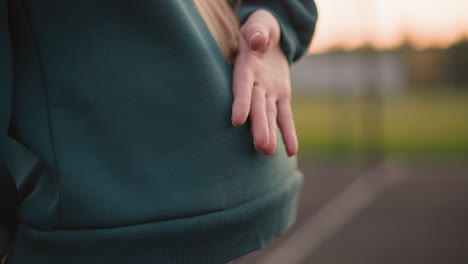 close-up waist view of lady slightly bent making gestures, two other ladies in background also slightly bent and blurred, participating in outdoor group fitness activity