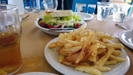 hand-held footage of a freshly prepared greek salad and a plate of chips, served within a outside restaurant