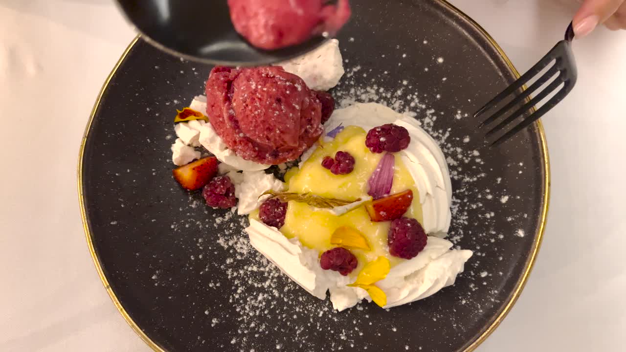 Delicious dessert on a plate with fruits and creme fresh, person eating with a spoon and fork