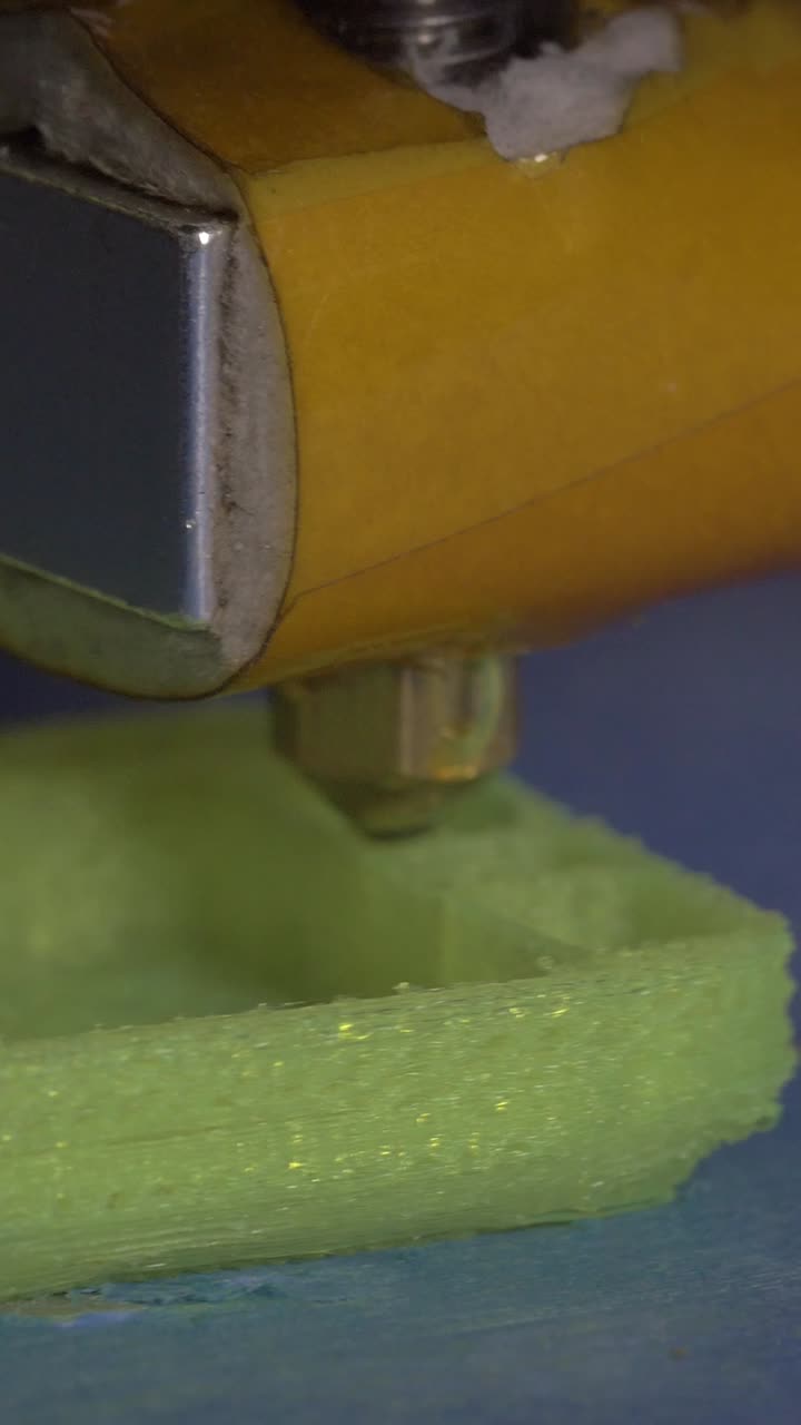 Primer plano de la boquilla de una impresora 3D extruyendo filamento de plástico verde