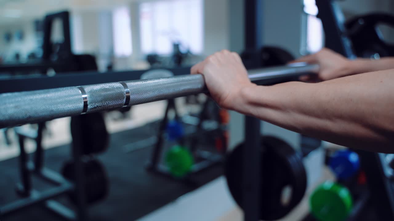 A woman puts her hands on the barbell in the gym opposite the mirror. Preparing to perform strength exercises. Blurred Background
