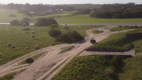 siguiente toma aérea de un vehículo rojo conduciendo por un camino rural a la ruta asfaltada durante la puesta de sol - chapadmalal,buenos aires