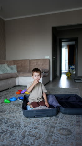 little caucasian toddler packing a big suitcase. kid puts some clothes into the case and then gets there himself. vertical video.