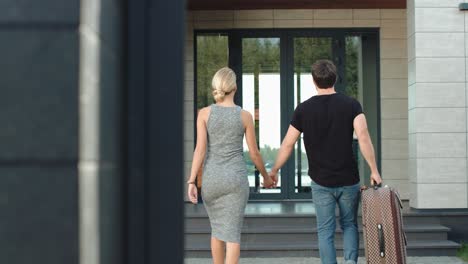 Traveler-couple-entering-hotel-back-view.-Modern-couple-coming-home-with-bag