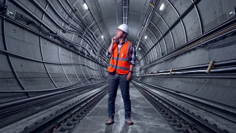 full body of asian male engineer with safety helmet thinking about something and looking around while standing in underground subway tunnel
