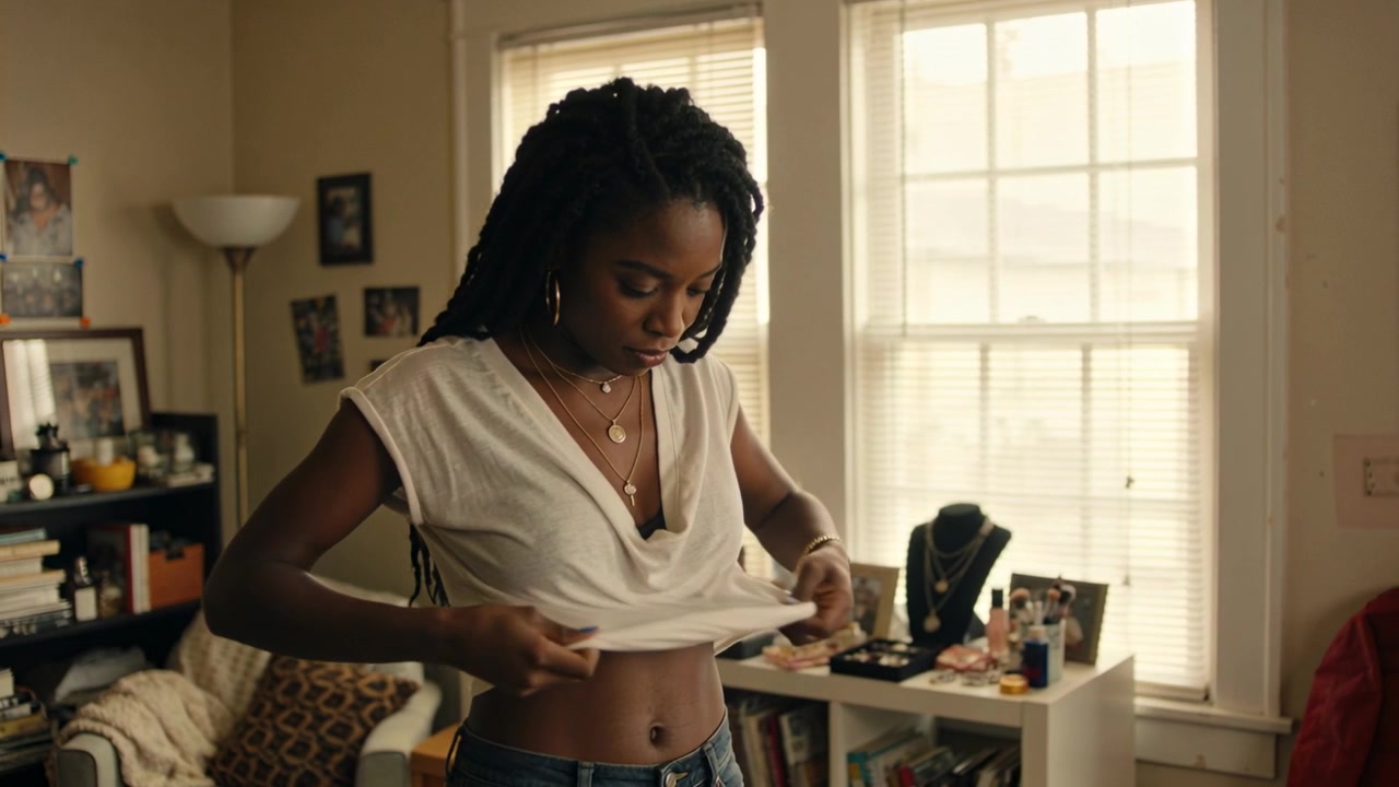 Adjusting woman feeling white tee uneven twisting front in bedroom, showing black bra and jeans