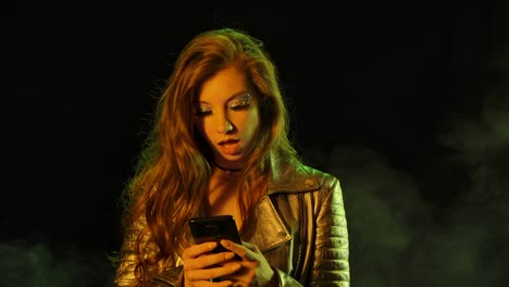 portrait of young pretty woman is joyfully texting on her phone then shows smartphone with a blue screen chroma key and points his finger at it. close up. slow motion