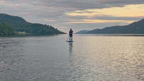 mujer joven en un traje de neopreno de pie en un stand up paddleboard en loch ness