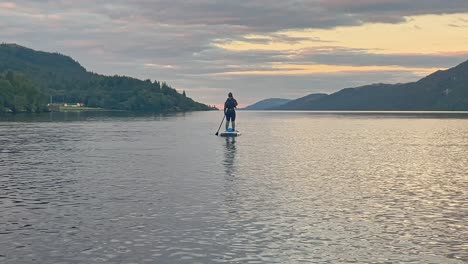 young woman in a wetsuit standing up on a stand up paddleboard on loch ness