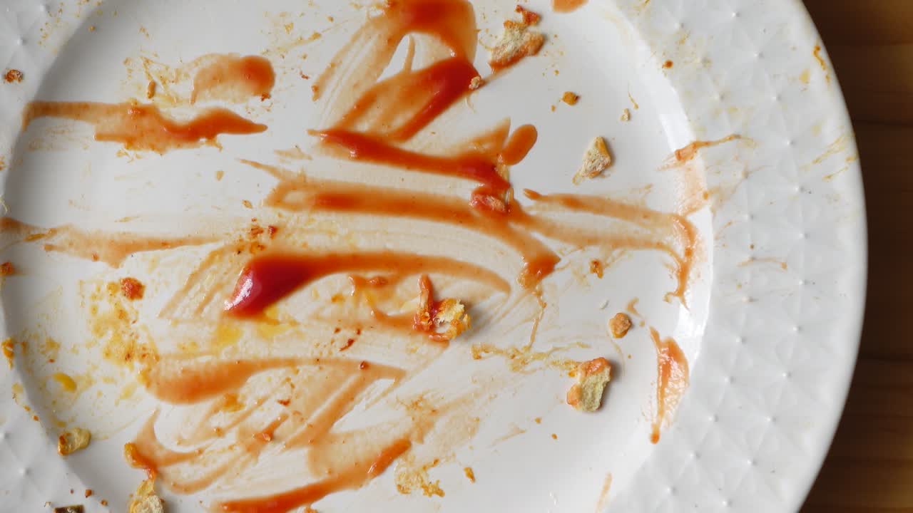 Piatto bianco sporco con ketchup e briciole su tavolo di legno