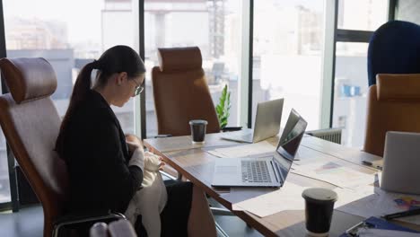 Confident-brunette-businesswoman-in-business-clothes-sits-at-an-office-desk-in-front-of-a-laptop-and-breastfeeds-her-nursing-baby-In-the-office