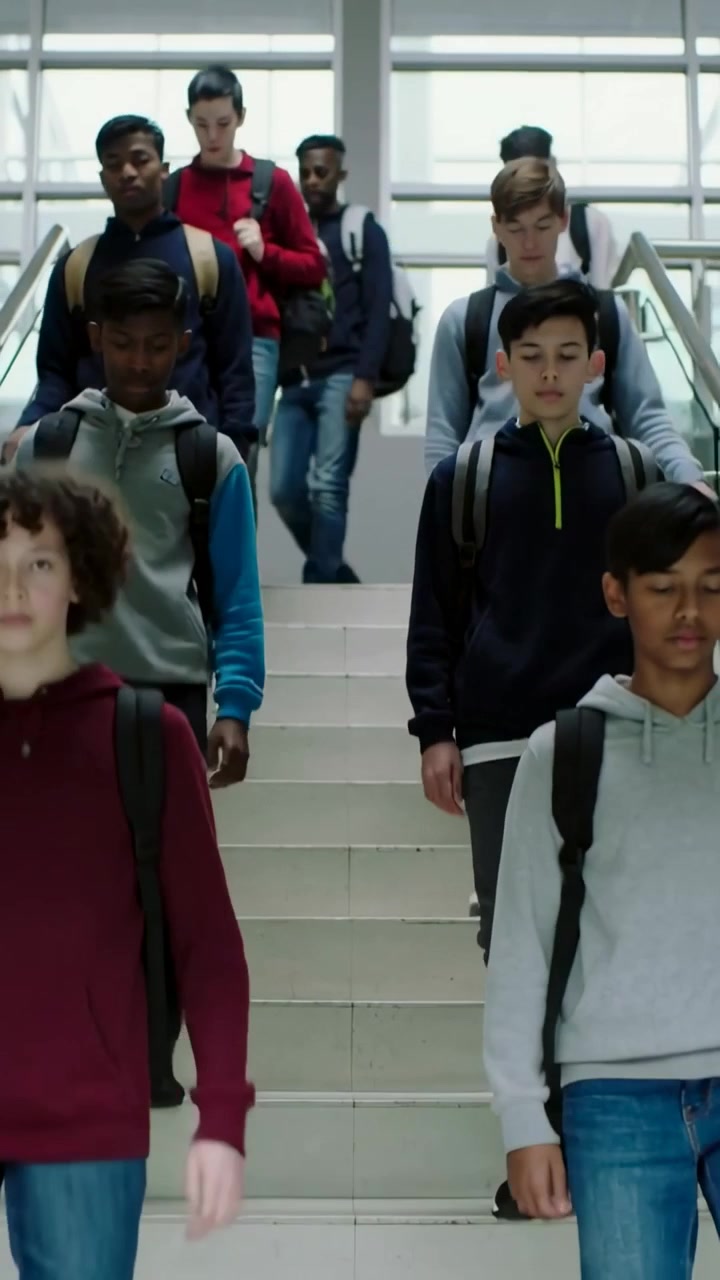Vertical video: Descending students wearing hoodies on school stairs, carrying backpacks to class