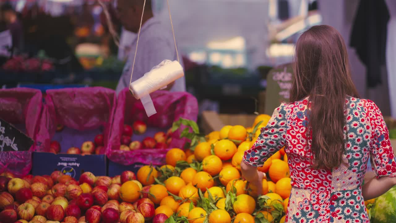mujer con cabello castaño yendo hacia el puesto de frutas en la feria para elegir uno de ellos