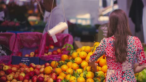 woman with brown hair going towards the fruit stand at the fair to choose one of them