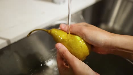 hände, die eine birne unter fließendem wasser waschen